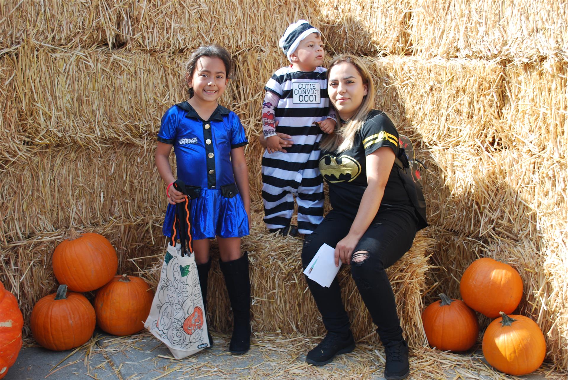 A woman is sitting on a bale of hay next to two children dressed in halloween costumes.
