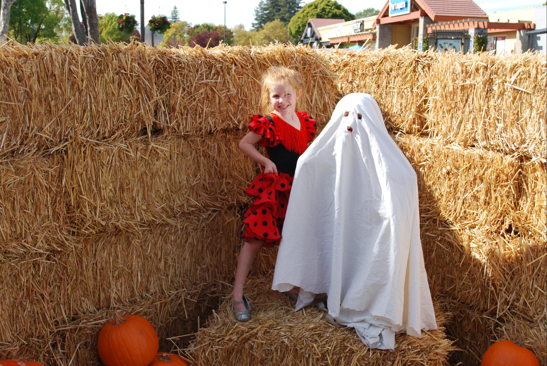 A little girl in a red dress is standing next to a ghost in a white sheet