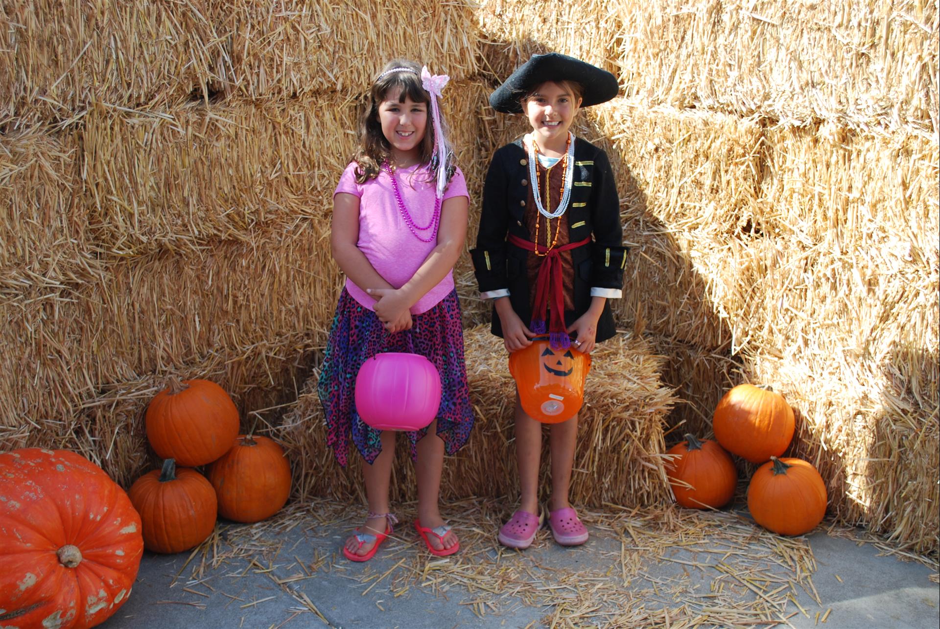 A boy and a girl are posing for a picture in front of hay bales and pumpkins
