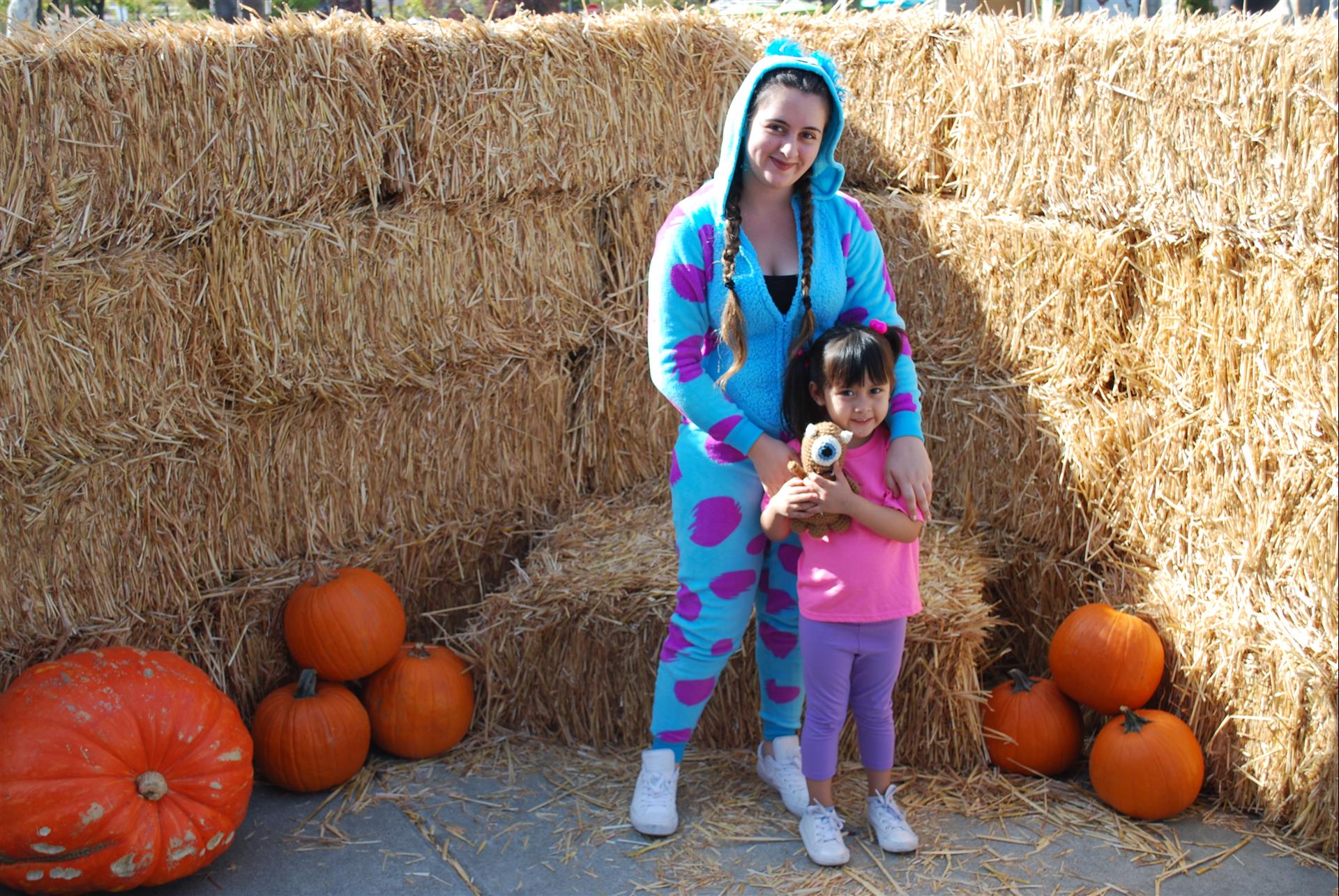 A woman and a little girl are posing for a picture in front of hay bales and pumpkins.