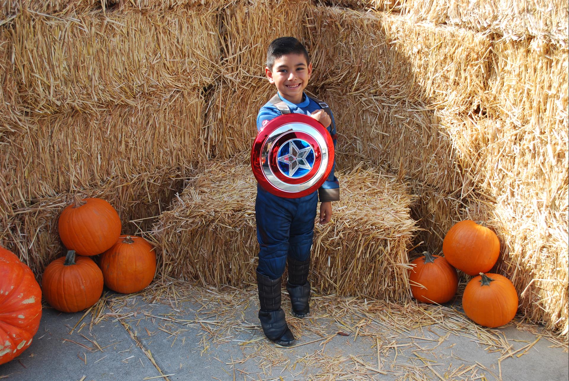 A young boy in a captain america costume is holding a shield.