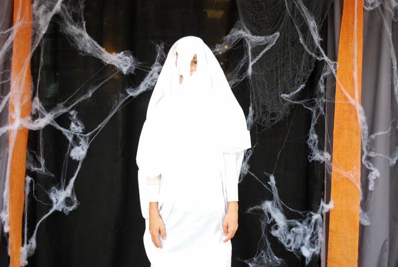 A person in a ghost costume is standing in front of a spider web.