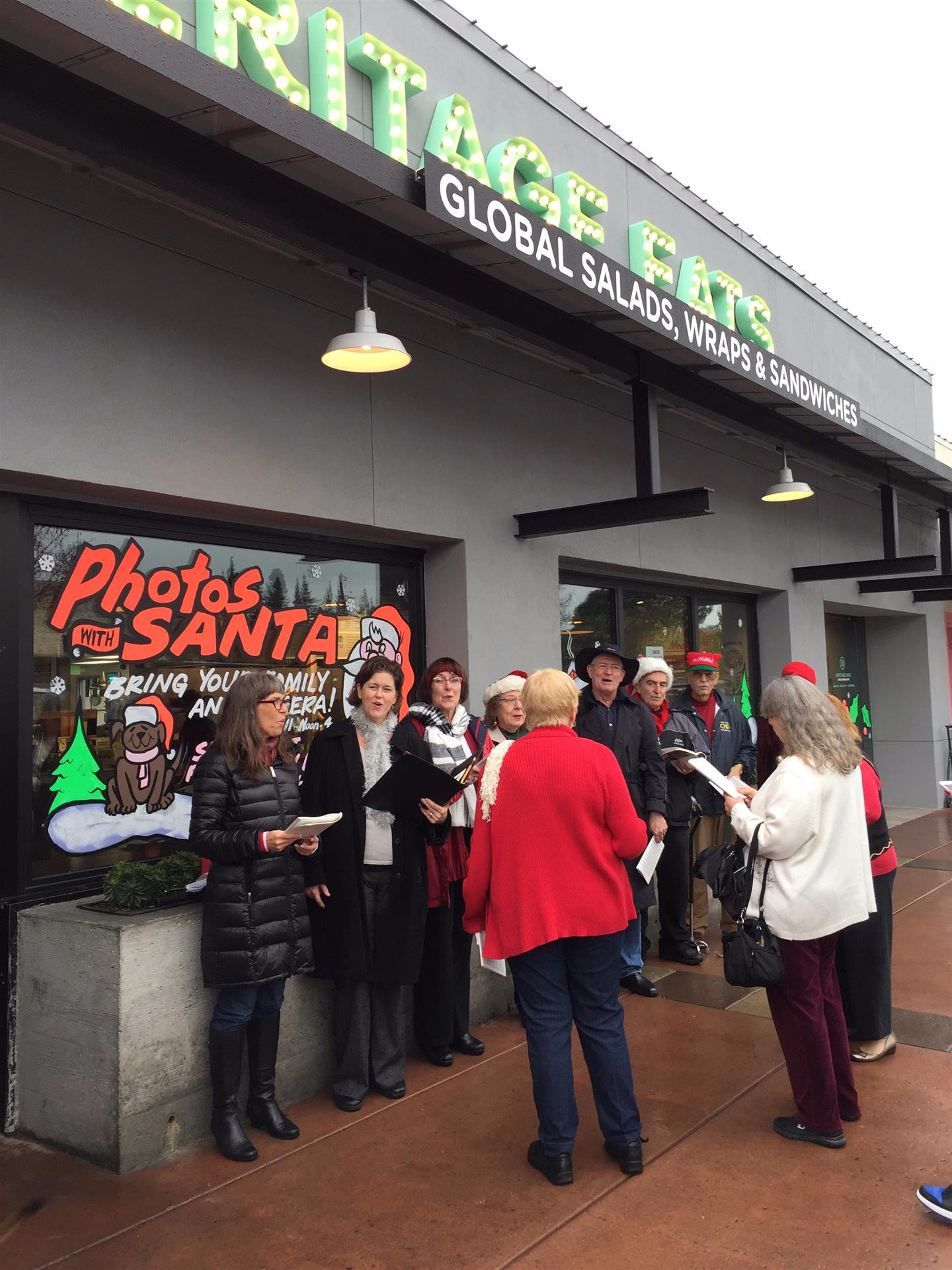 A group of people are standing outside of a restaurant called photos santa