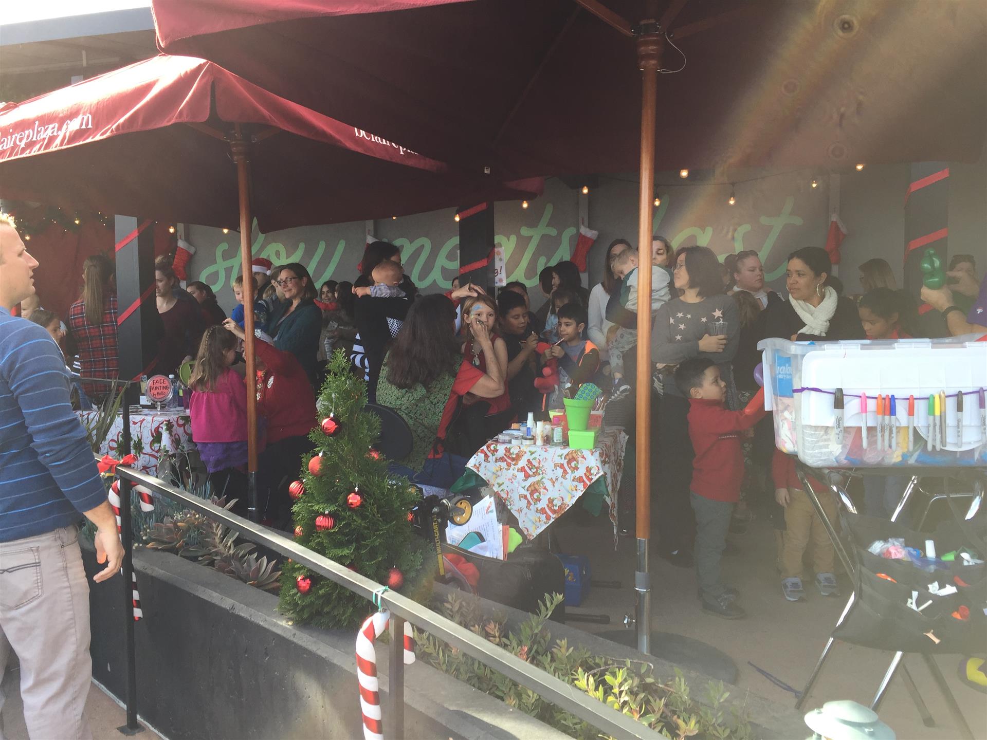 A group of people are standing under an umbrella in front of a christmas tree.