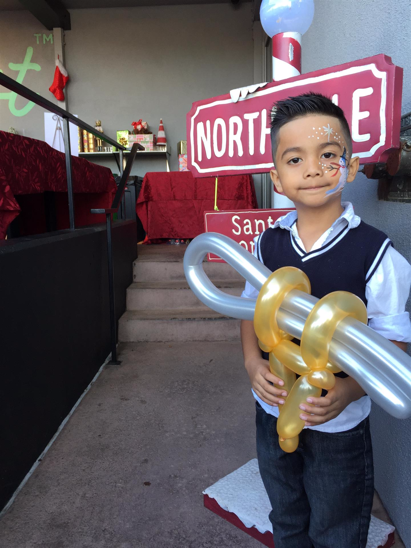 A young boy is holding balloons in front of a north pole sign