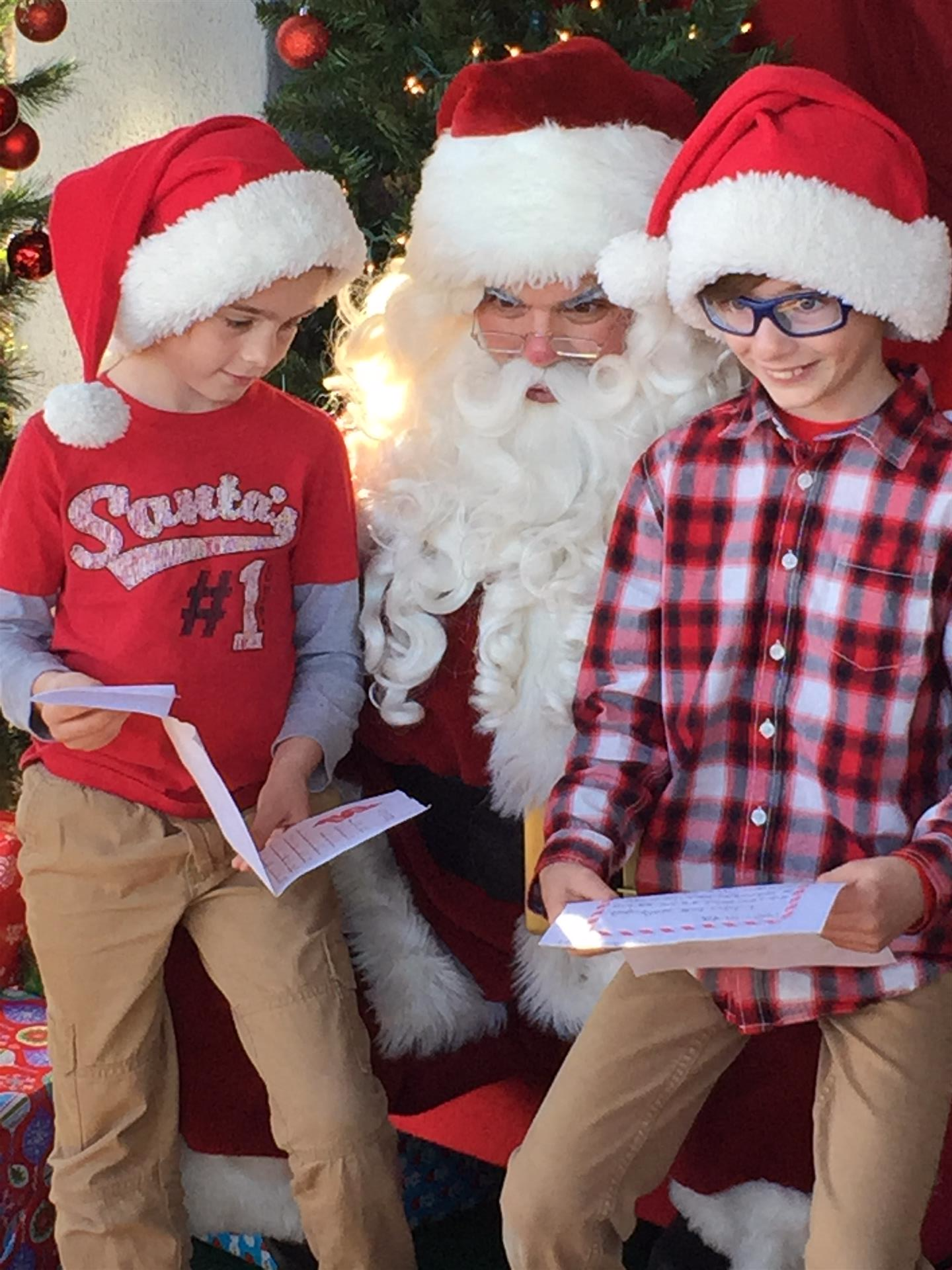 Two boys wearing santa hats are sitting next to santa