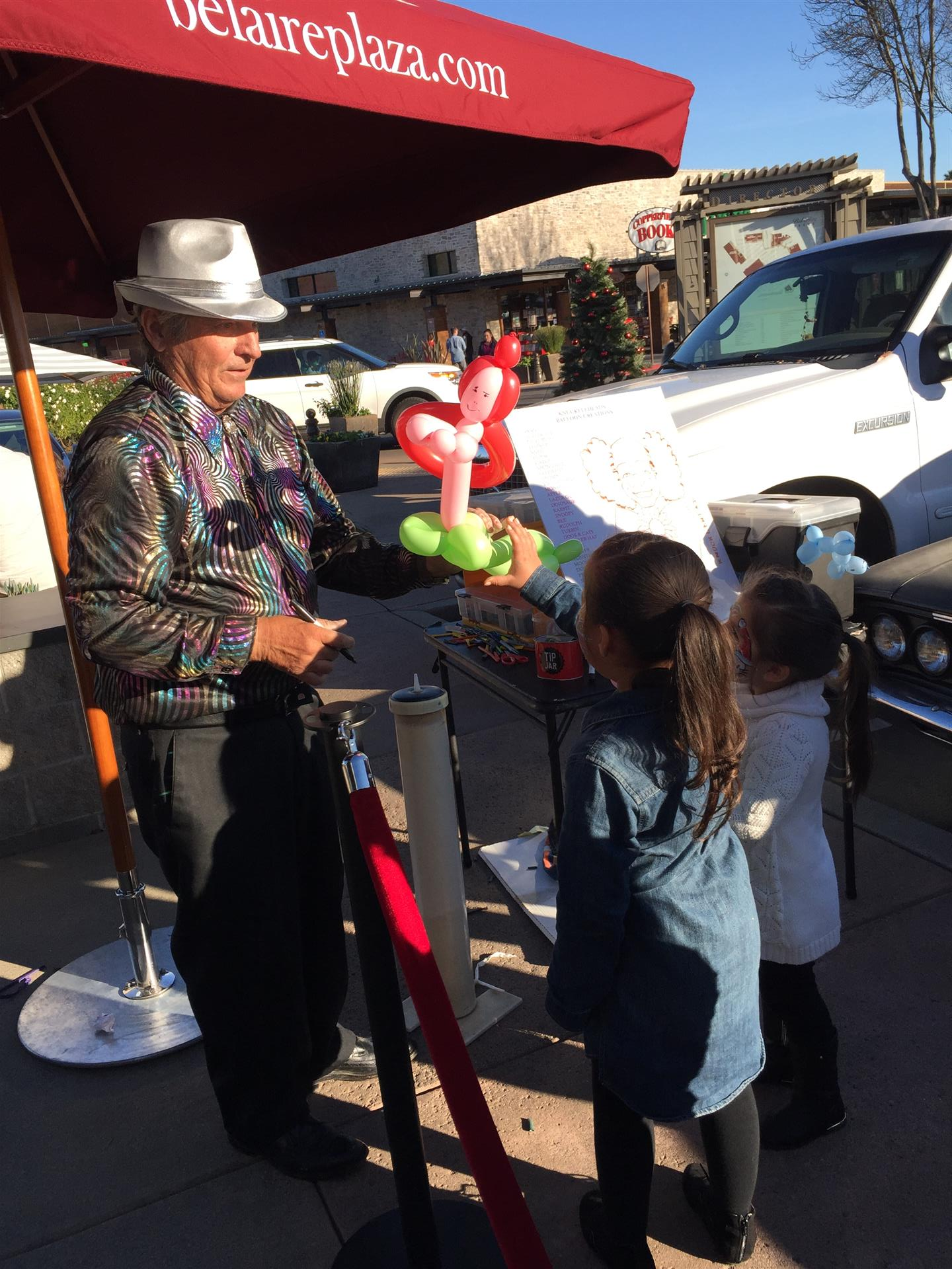 A man is holding balloons in front of a red umbrella.
