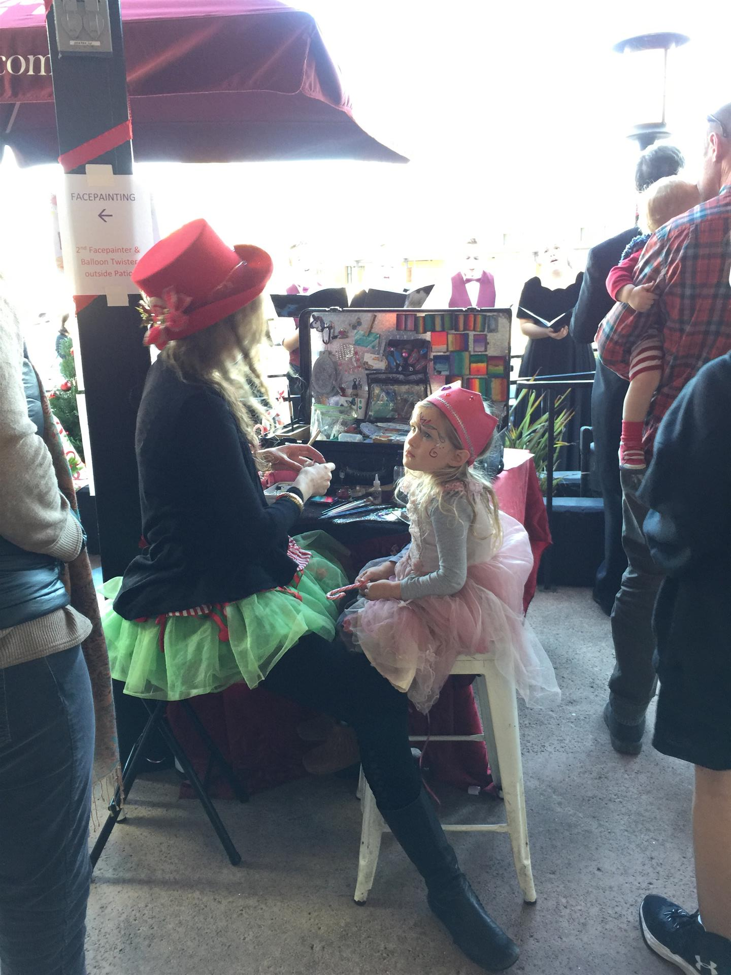 A woman in a red hat is sitting next to a little girl in a pink tutu.