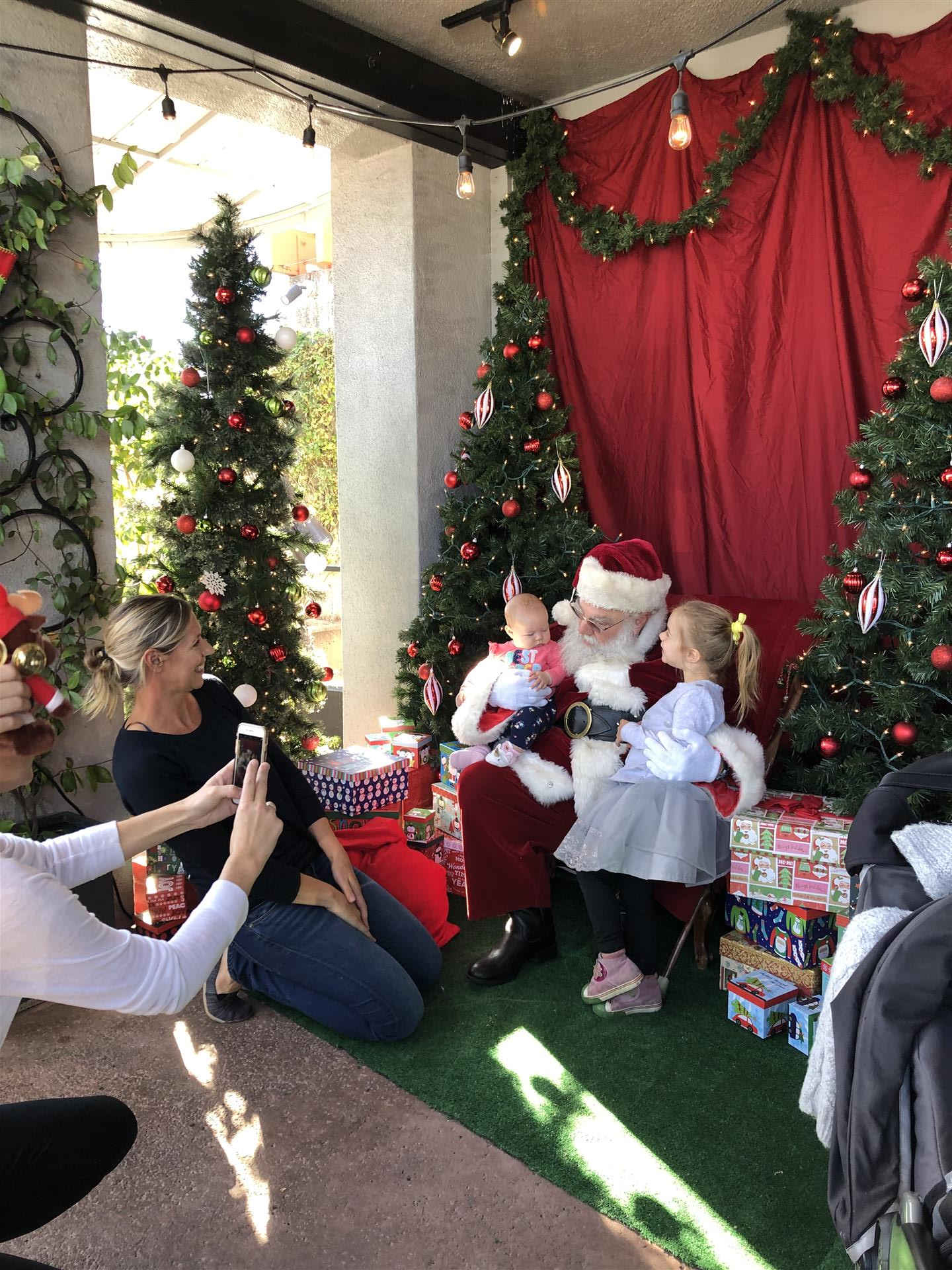 A woman is taking a picture of a little girl sitting on santa 's lap.