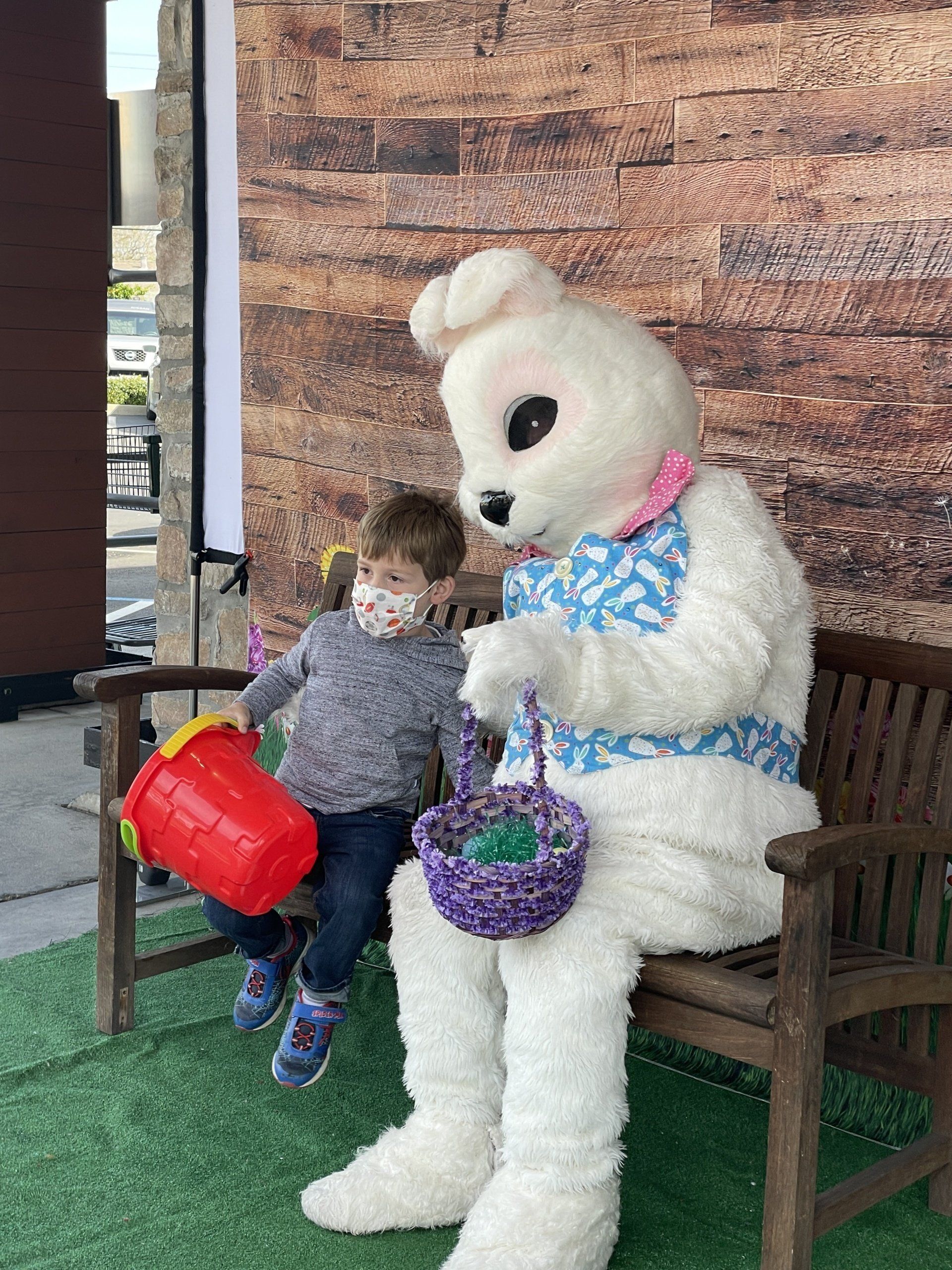 A little boy is sitting next to an easter bunny on a bench.
