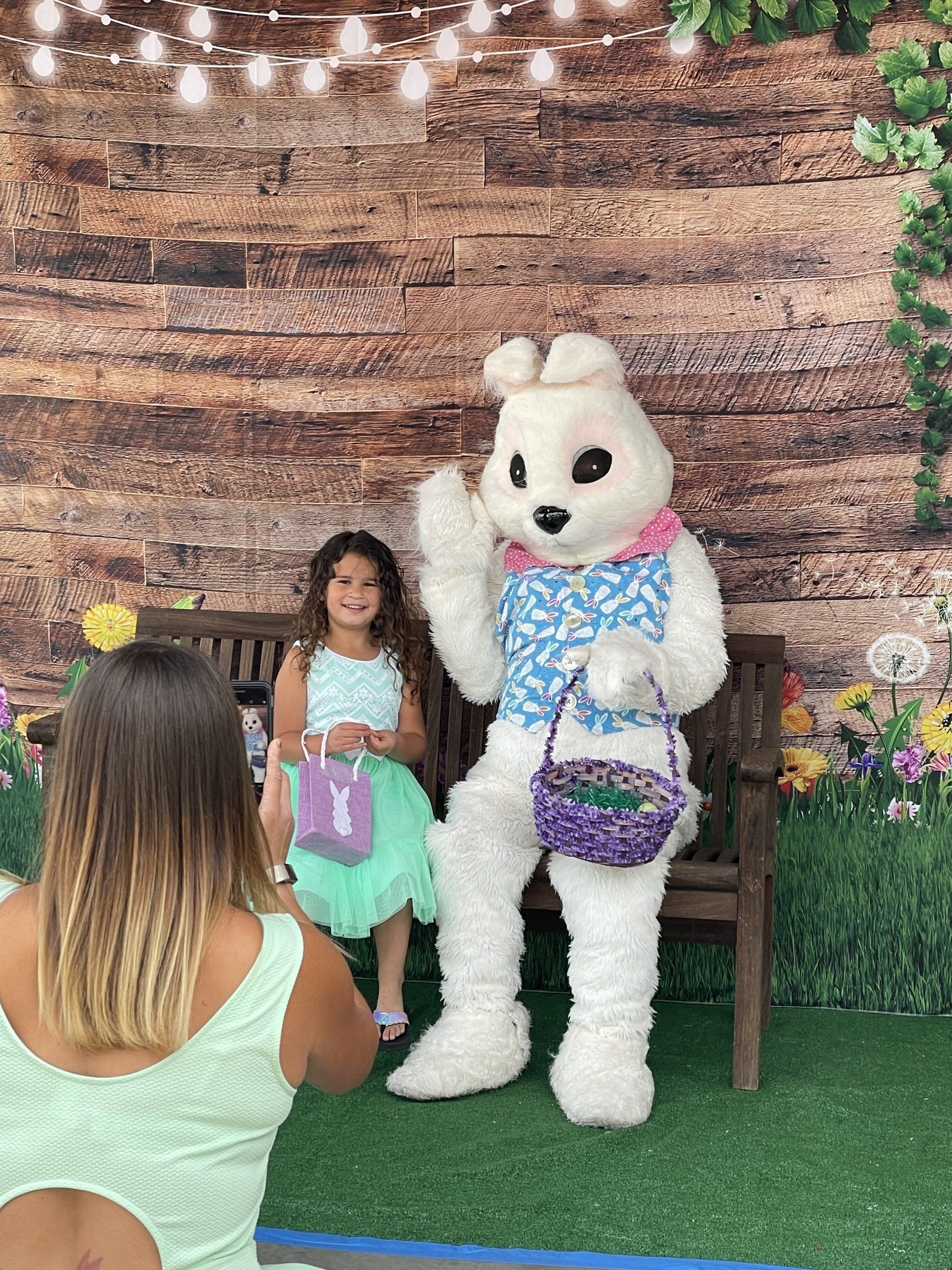 A woman is taking a picture of a little girl and an easter bunny.