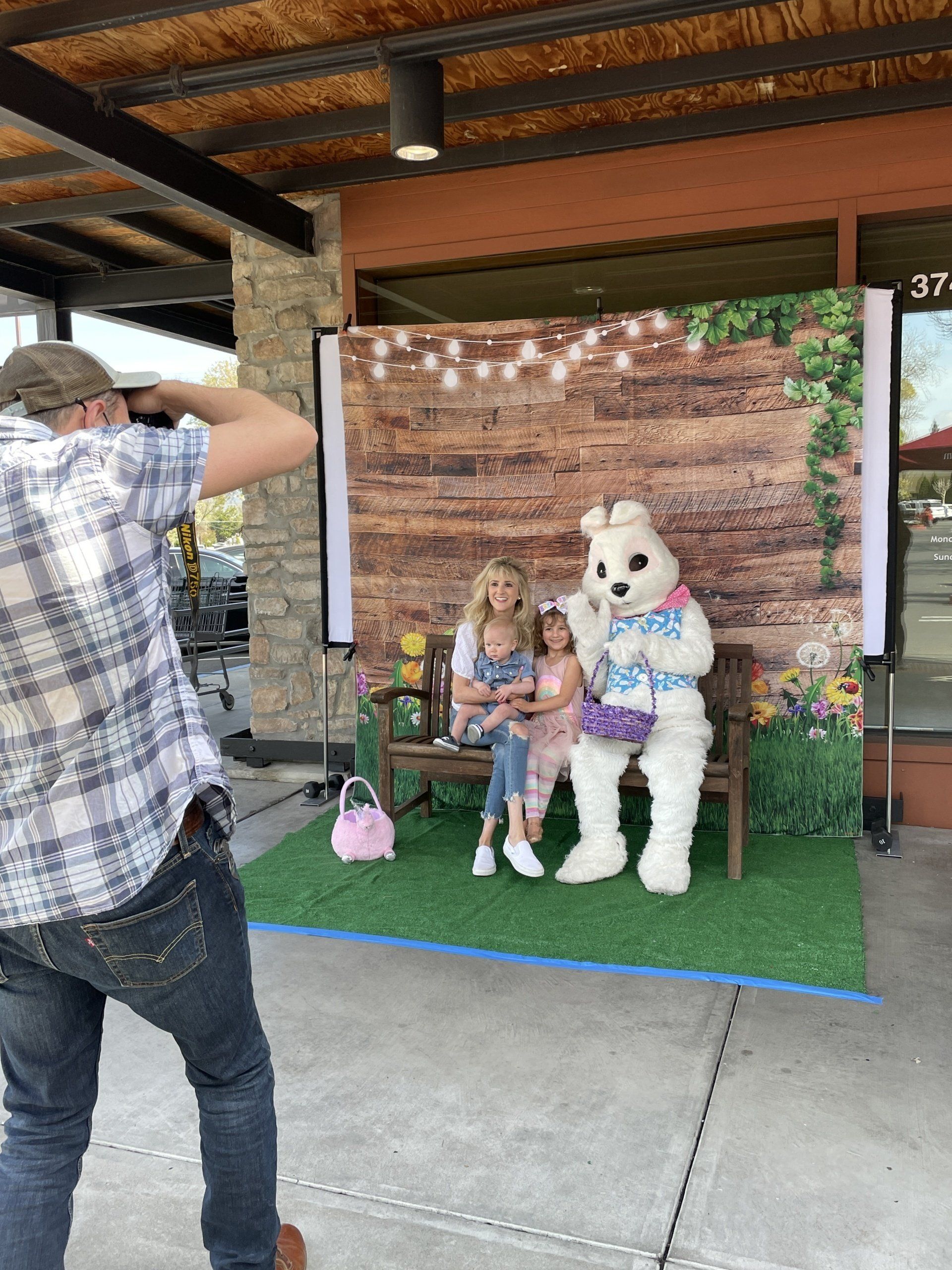 A man is taking a picture of a woman sitting on a bench with an easter bunny.