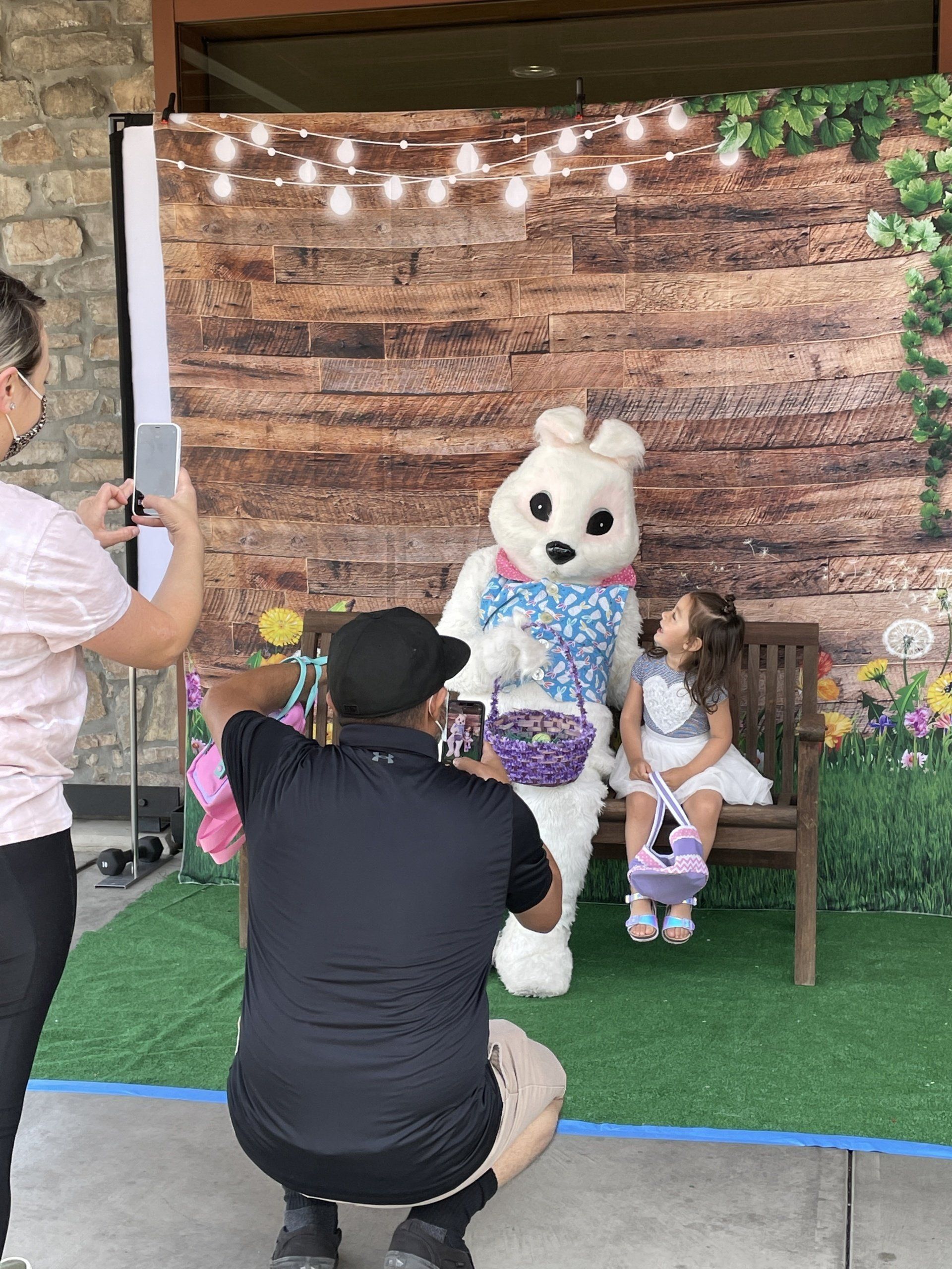 A man is kneeling down to take a picture of a little girl and an easter bunny.