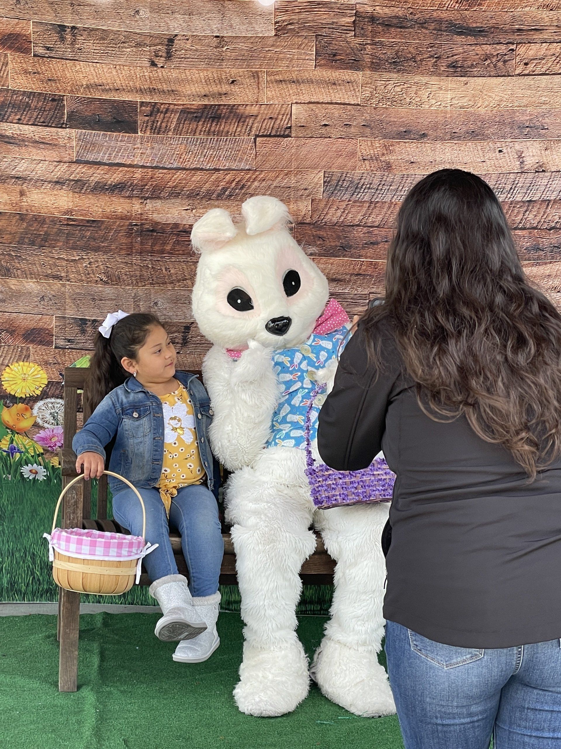 A woman is taking a picture of a little girl sitting next to an easter bunny.