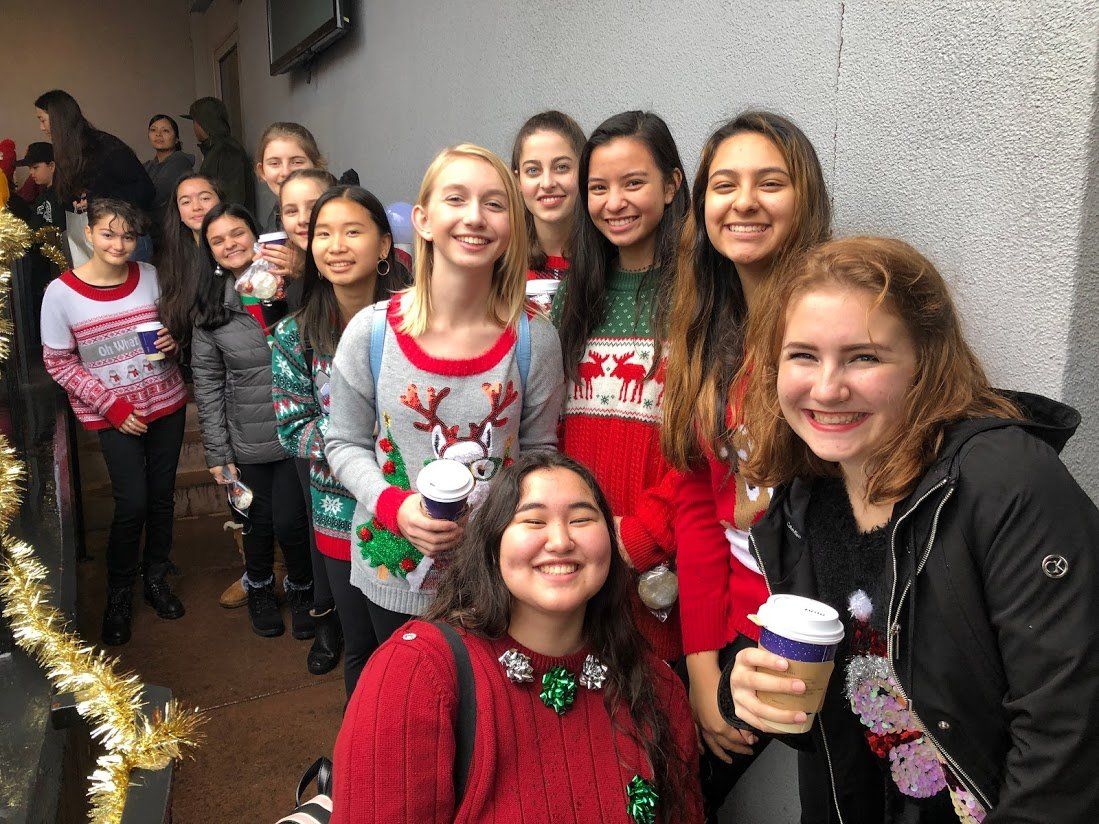 A group of young women wearing christmas sweaters are posing for a picture.