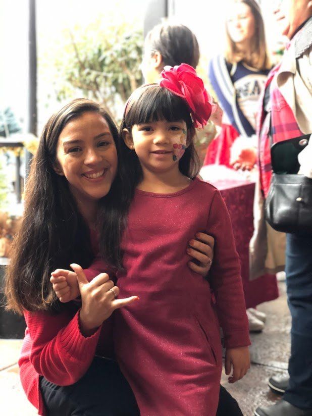 A woman in a red shirt is holding a little girl in a red dress.