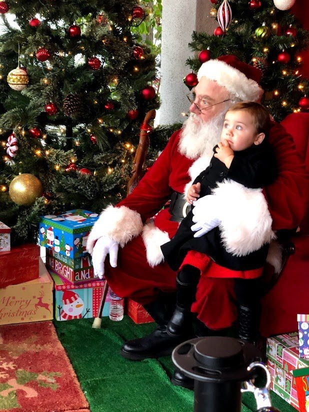 A little boy is sitting on santa 's lap in front of a christmas tree