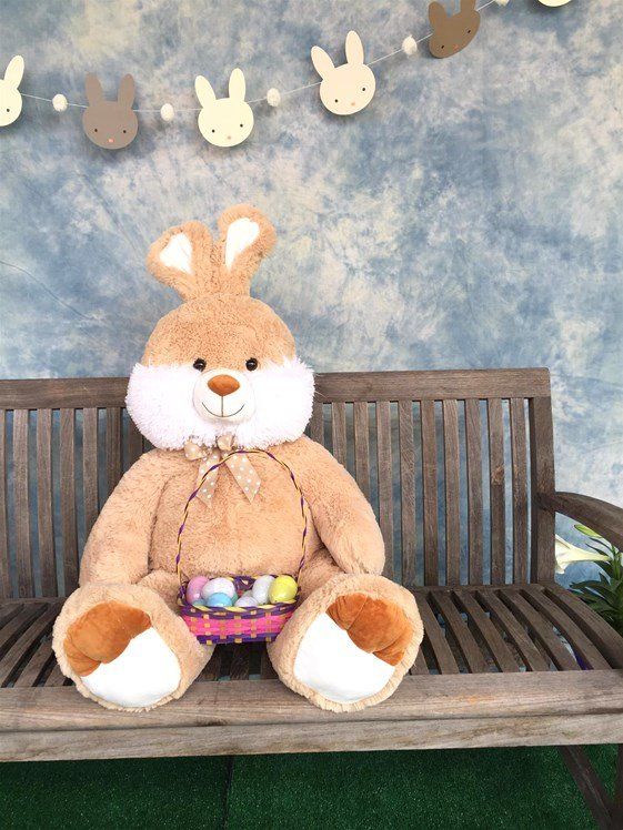 A stuffed bunny is sitting on a wooden bench with a basket full of easter eggs.
