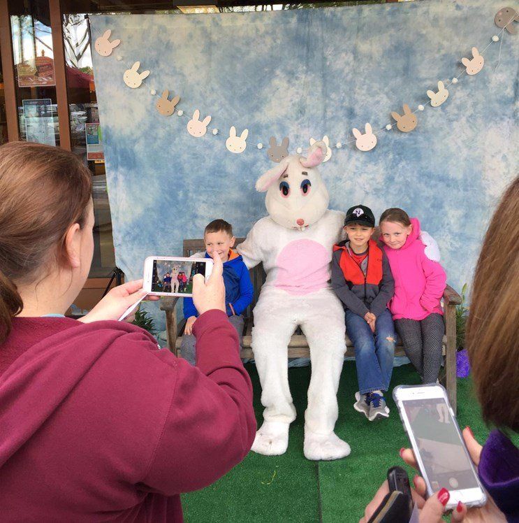 A woman is taking a picture of a group of children and a bunny mascot