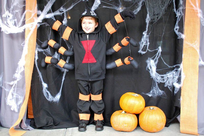 A child in a black widow costume stands in front of pumpkins