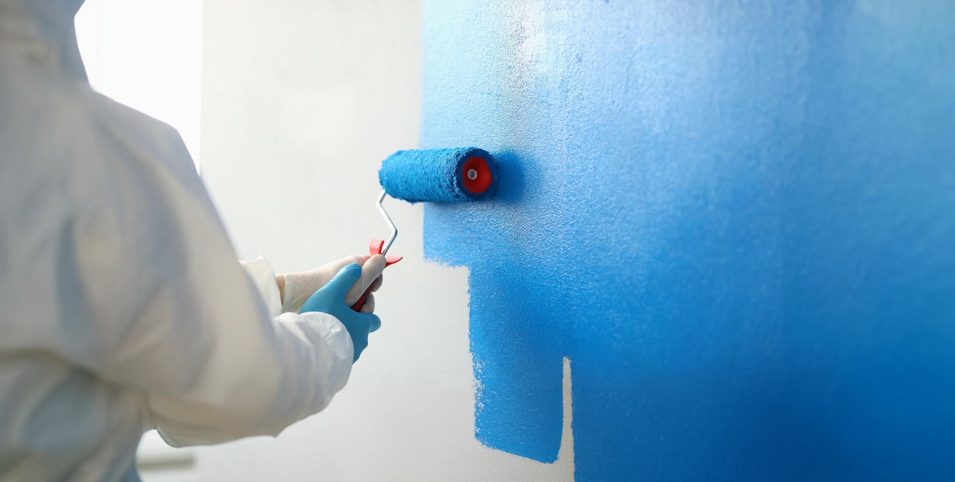 A person is painting a wall with a blue paint roller.