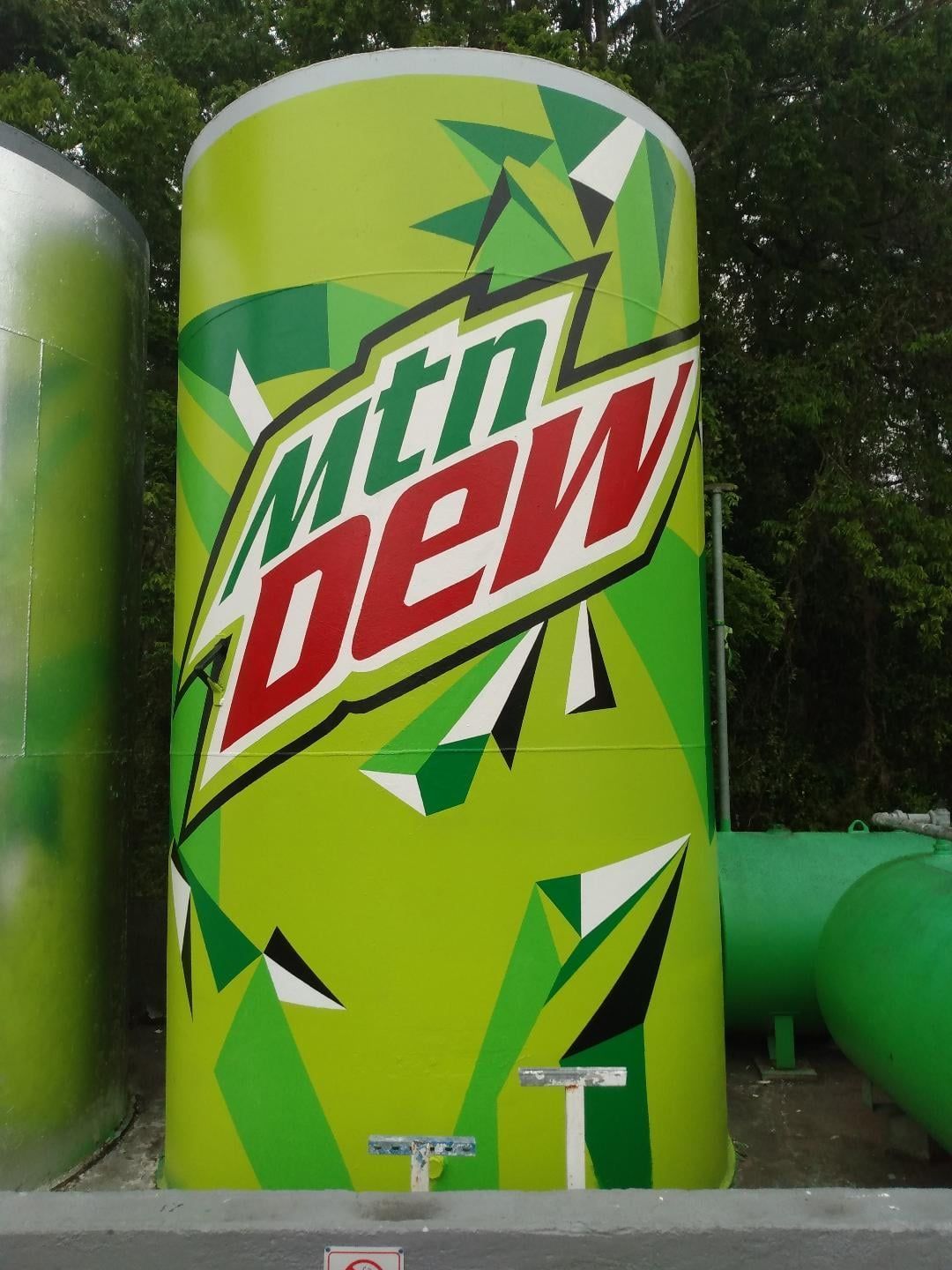 A large can of mtn dew sits in front of some green pipes