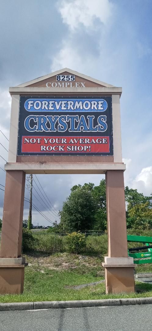 A large sign that says `` forevermore crystals '' is sitting in the middle of a grassy field.