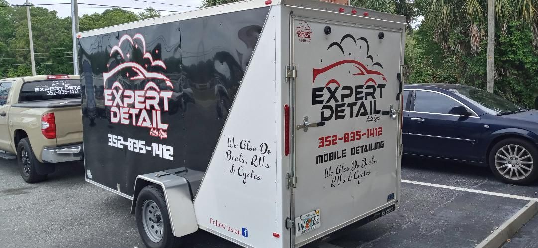 A trailer with the word expert detail on it is parked next to a truck.
