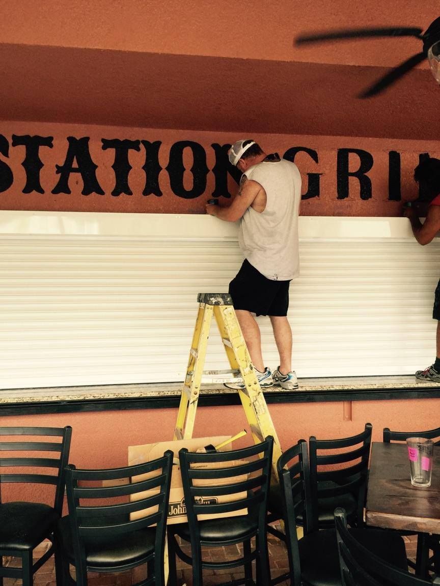 A man standing on a ladder in front of a sign that says station grill