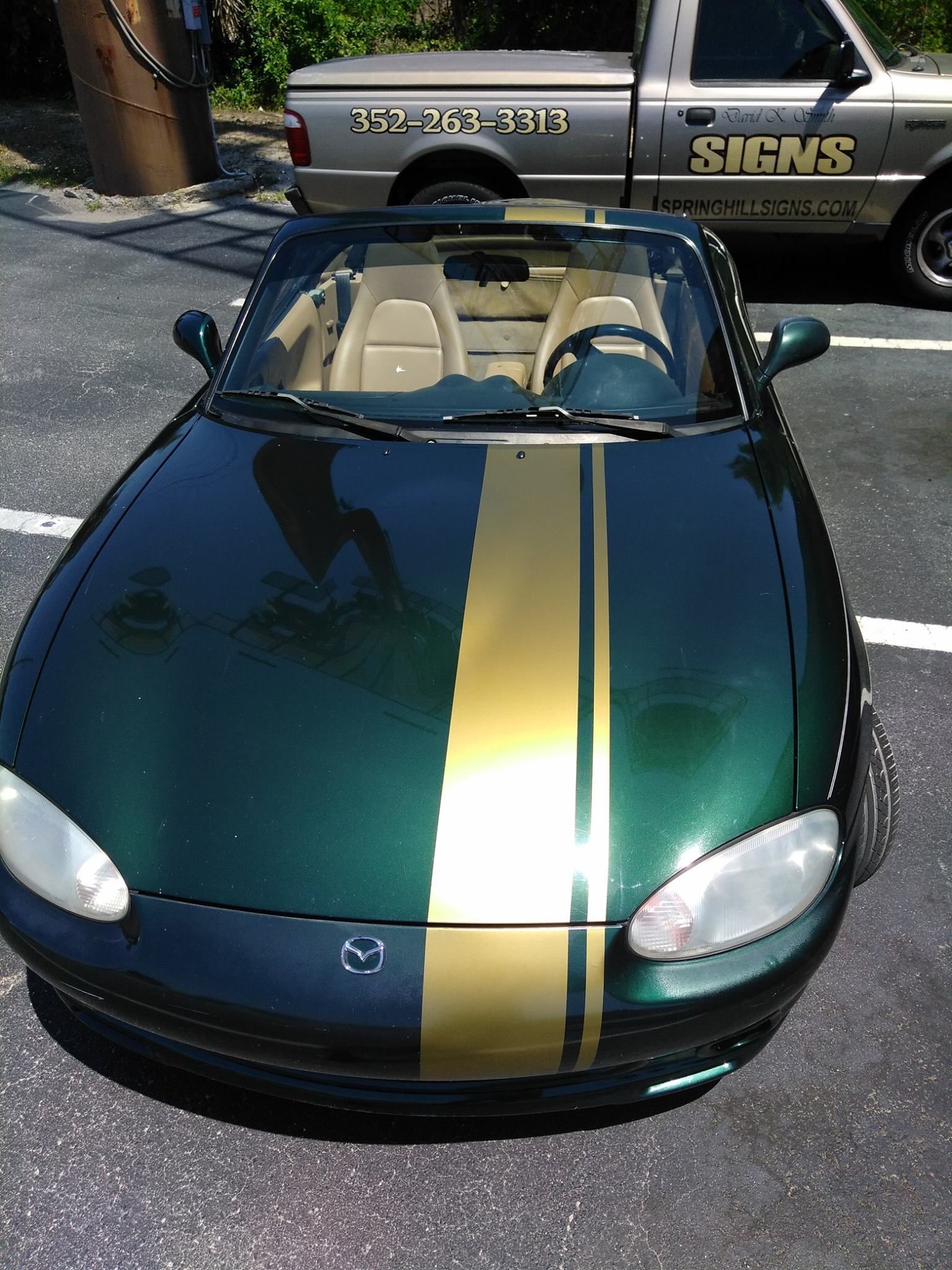 A green sports car is parked in front of a signs truck