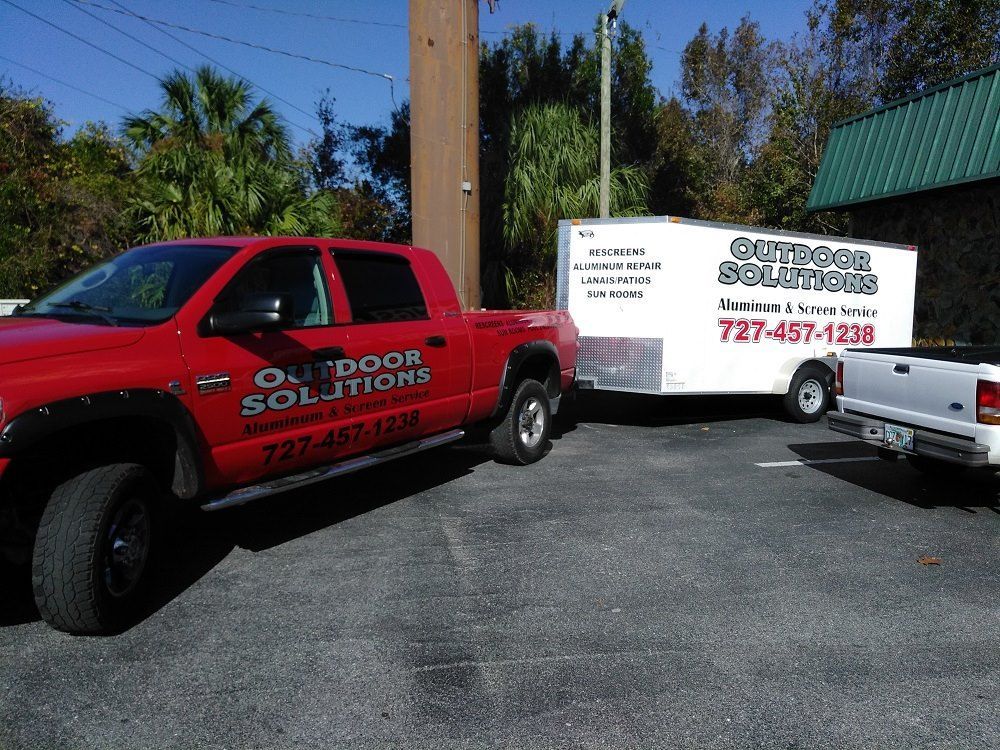A red truck that says outdoor solutions is parked next to a white truck