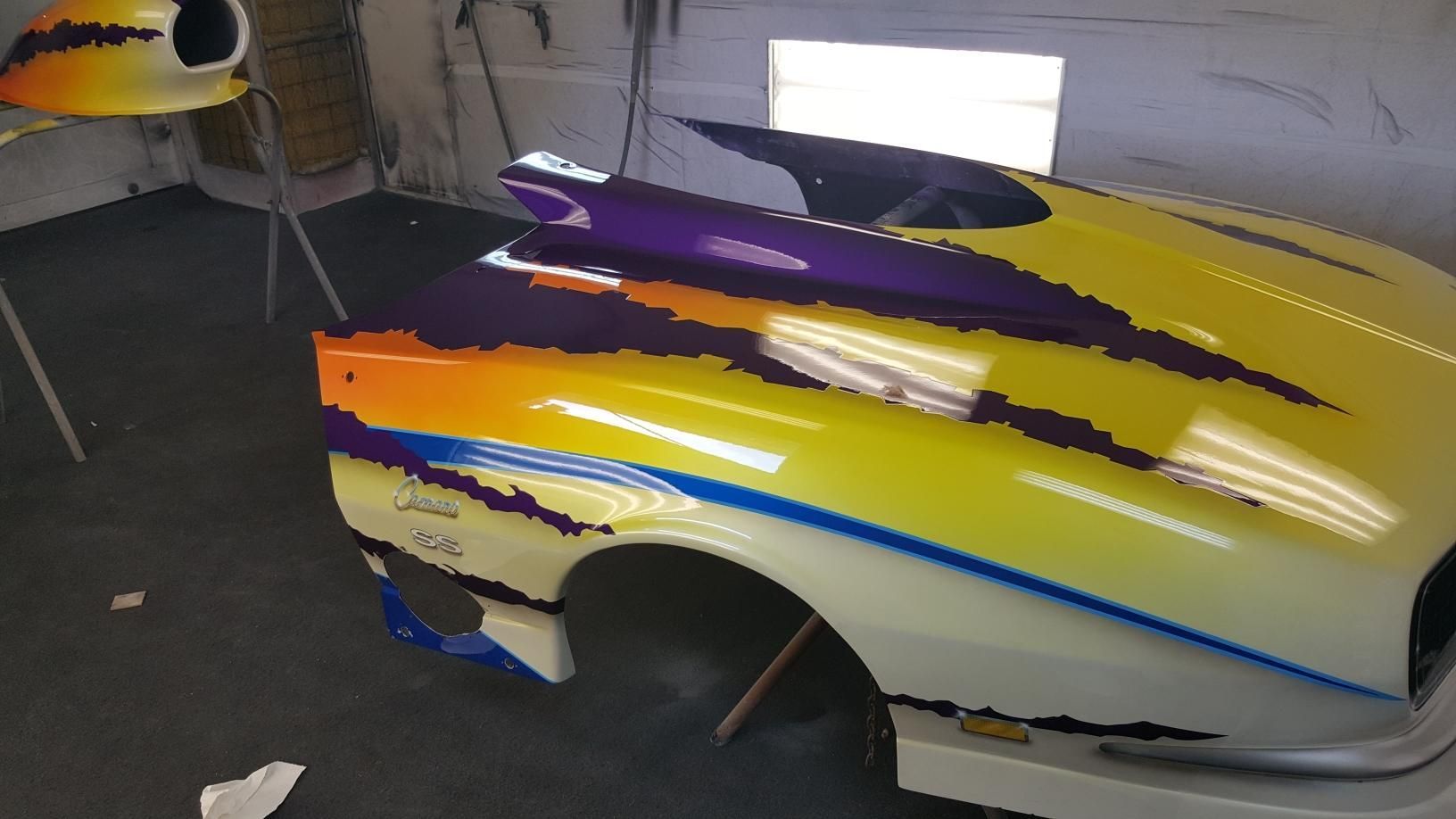 A yellow and purple car is painted in a garage