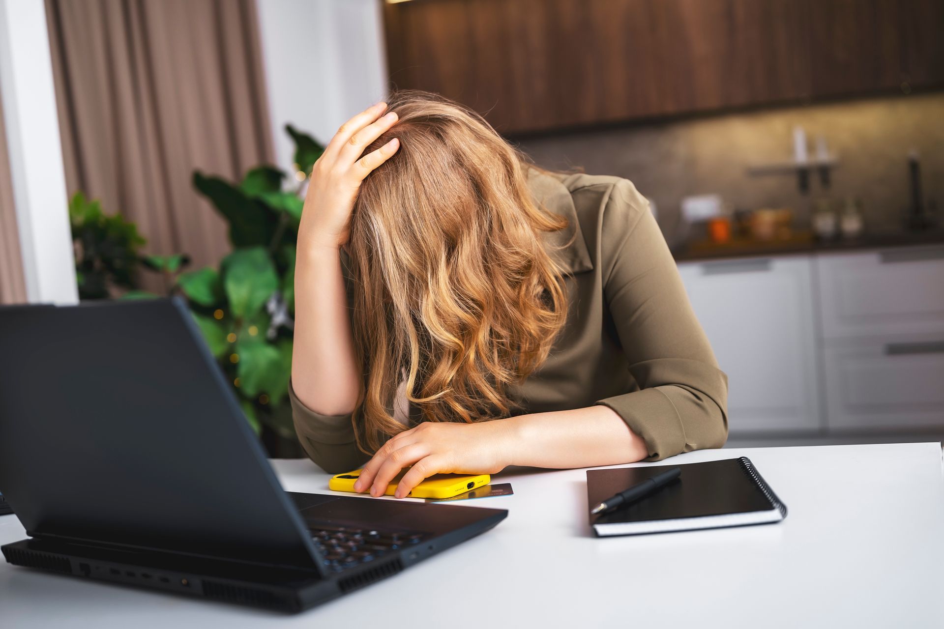 Woman with glasses, orange shirt, stressed at a table with bills, calculator, and laptop.