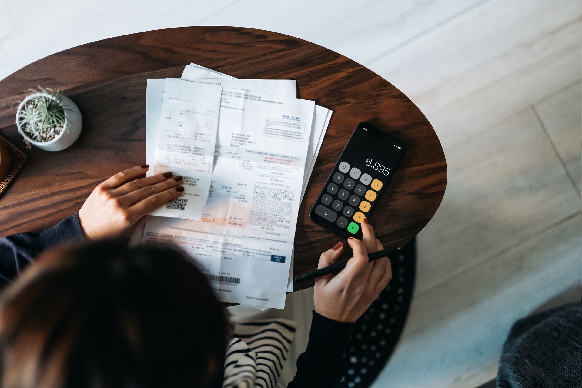 Person calculating expenses on a phone, with bills spread on a table.