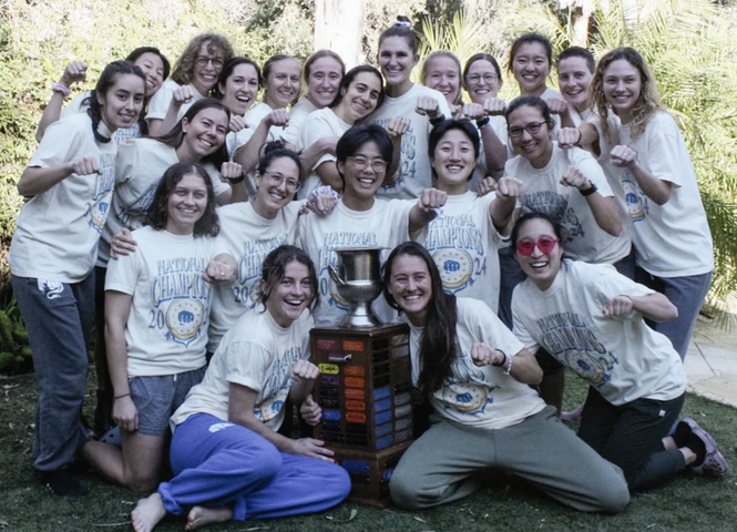 Group of smiling people in white shirts posing outdoors around a colorful stacked cube sculpture.