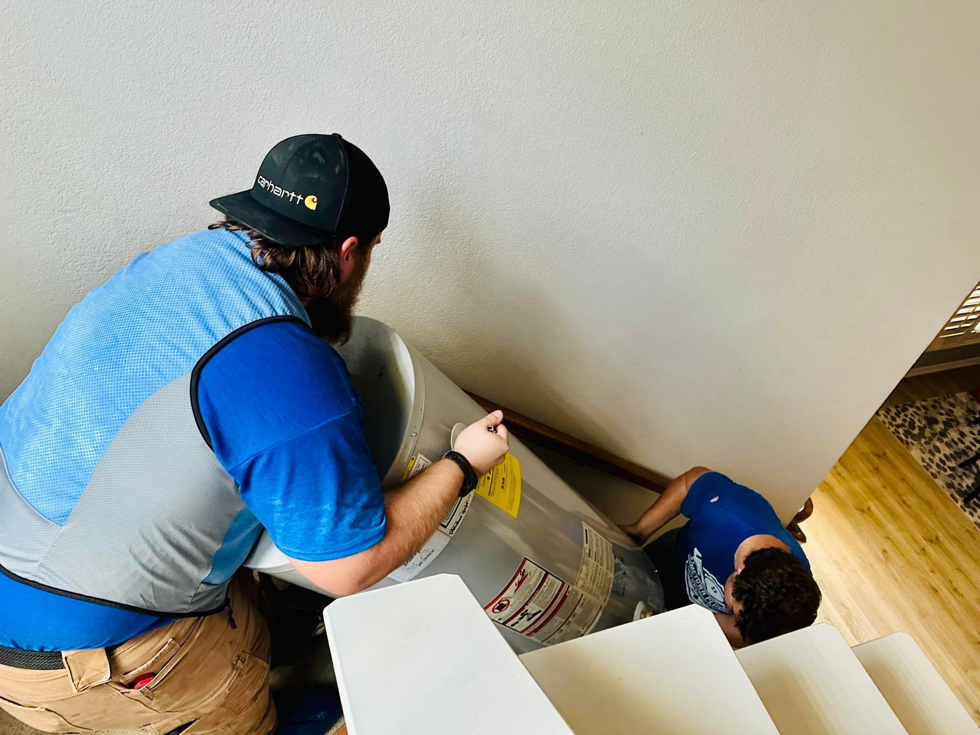 Two people carrying a water heater up a flight of stairs.
