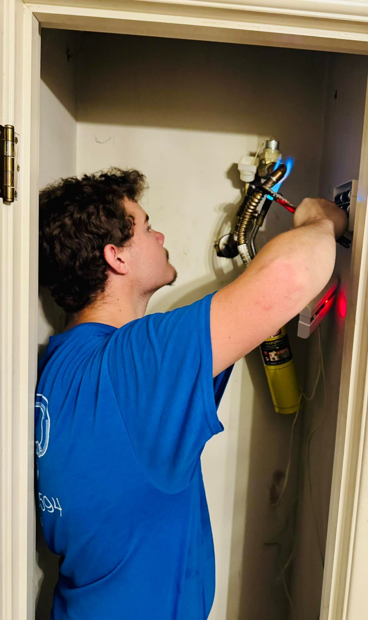 Man in blue shirt working on electrical wiring in a closet, using tools.