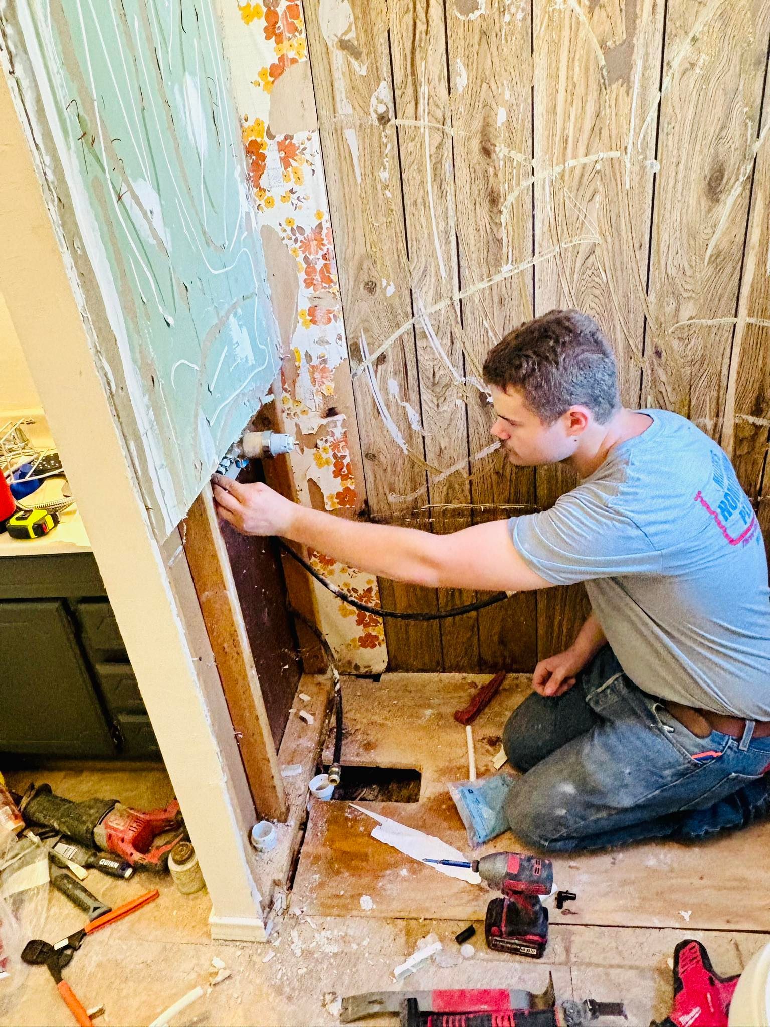 Person installing plumbing in a bathroom renovation, surrounded by tools and exposed wall framing.