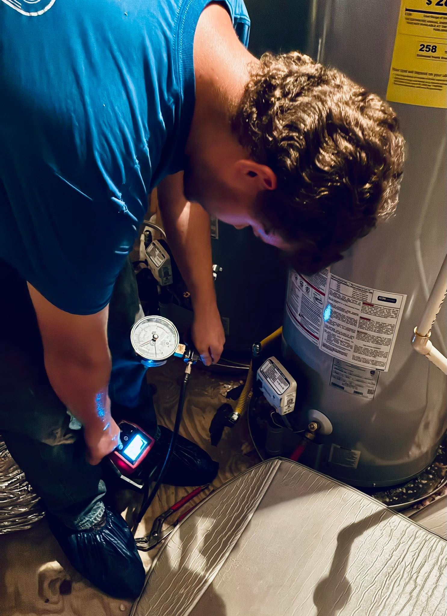 Person in blue shirt working on a water heater, using tools in an indoor setting.