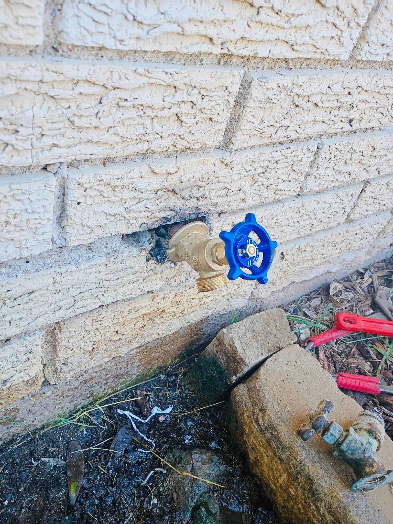 Outdoor water spigot with blue handle, mounted on a brick wall.