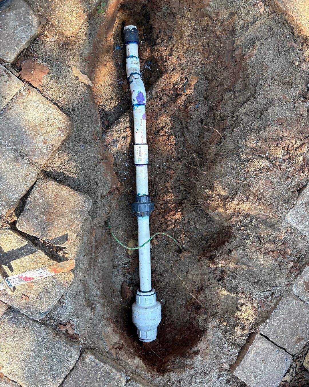 PVC pipes in a trench, possibly for irrigation or plumbing. A green wire is also present.