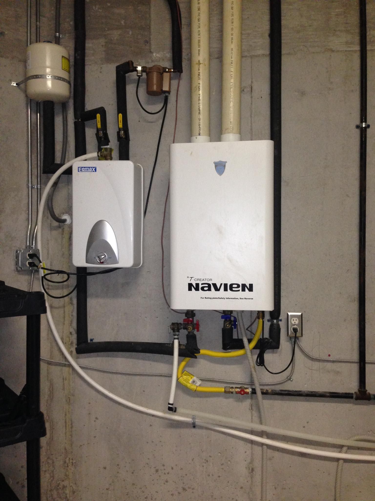 Two white water heaters mounted on a gray concrete wall with black pipes and yellow gas lines.