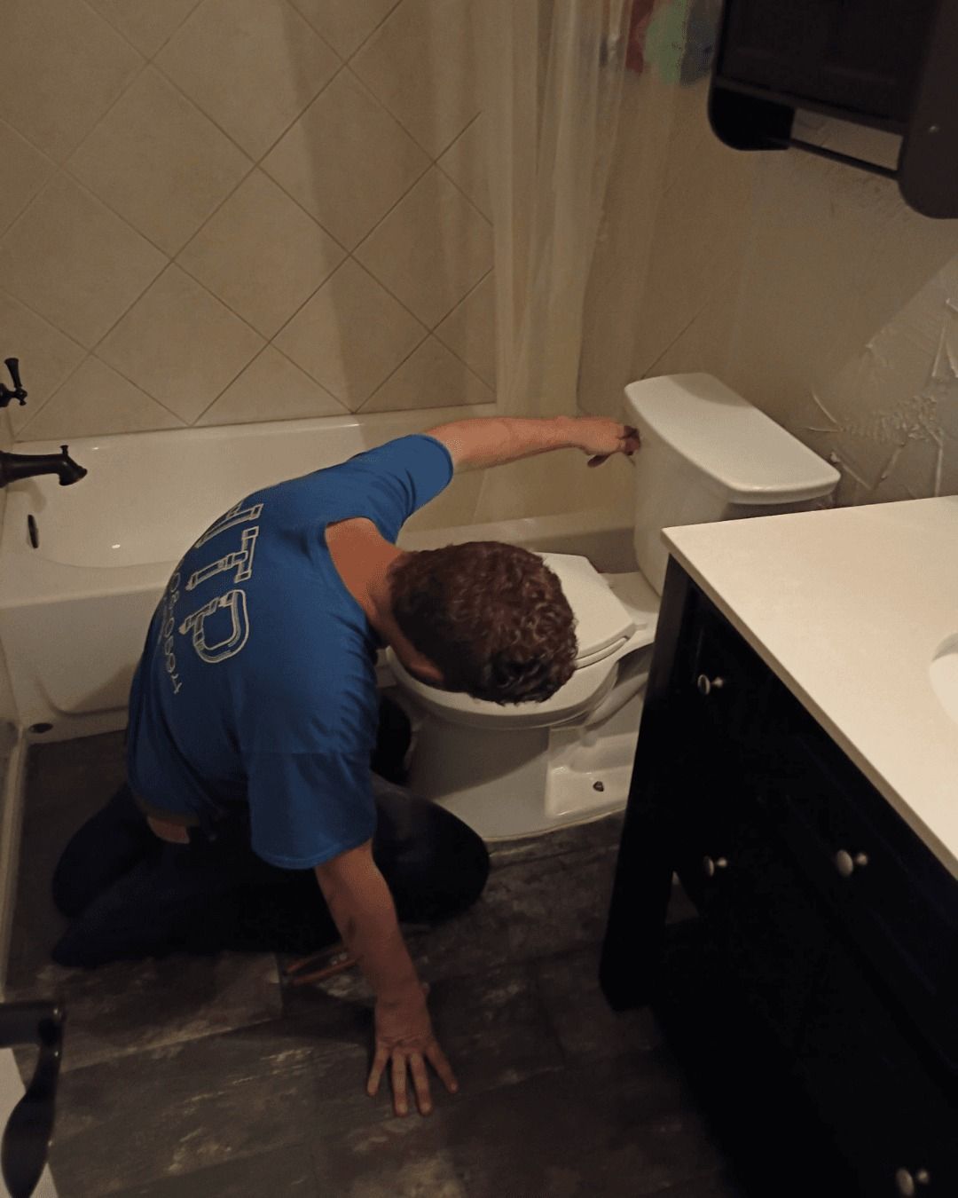 Person installing a toilet in a bathroom with a white tub and black vanity.