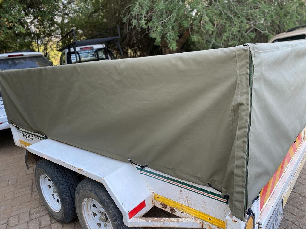 A trailer with a green tarp on it is parked in a driveway.