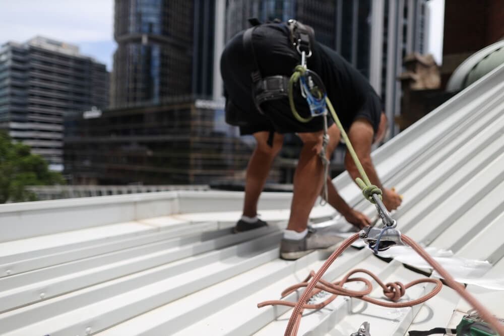 Roofer in Harness Inspecting Metal Roof