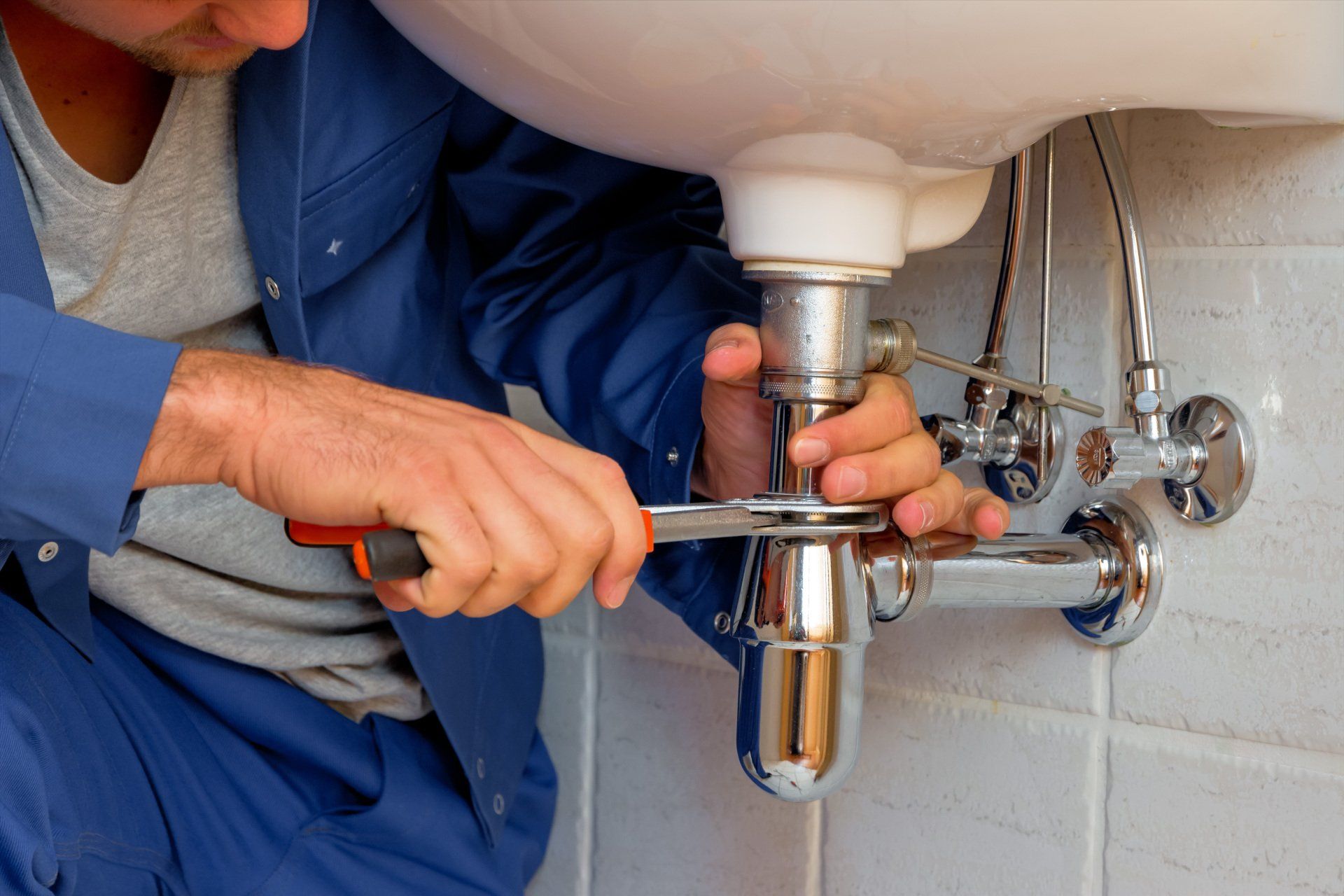 Plumber in Blue Uniform Using a Wrench to Work on Pipes — Mid Richmond Plumbers & Suppliers in Brunswick Heads, NSW