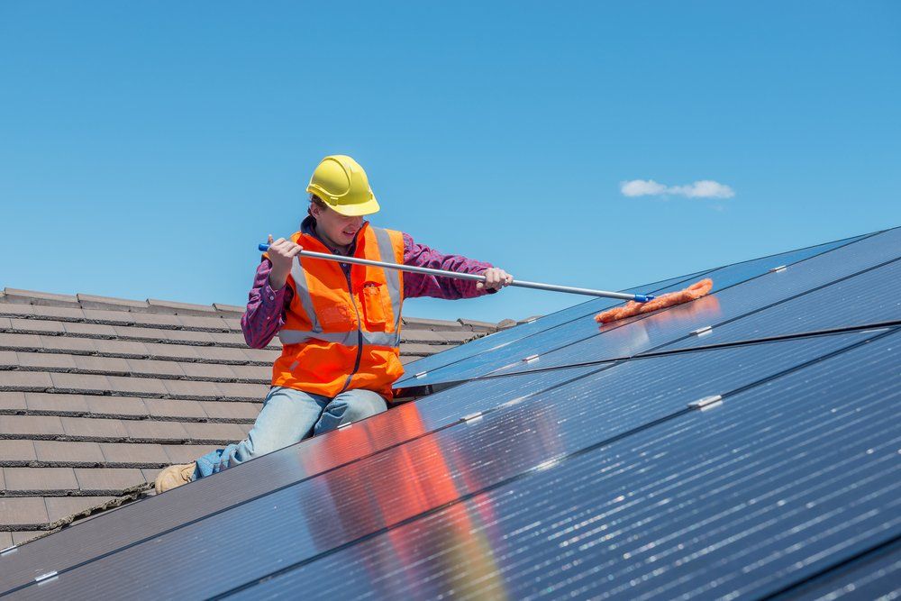 A Man is Cleaning Solar Panels on the Roof of a House — Mid Richmond Plumbers & Suppliers in Casino, NSW