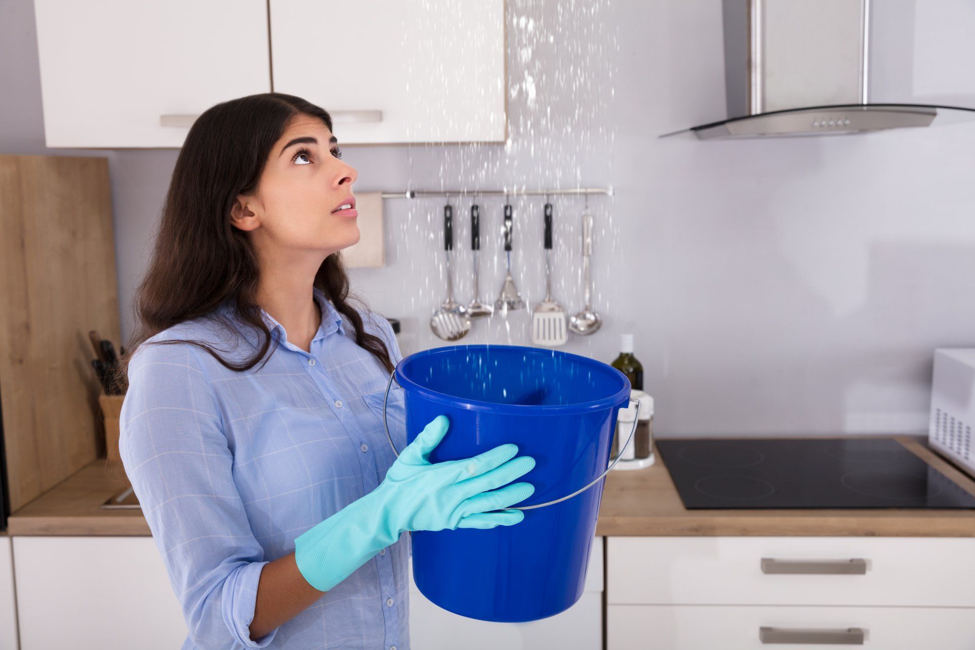 woman holding bucket under leak with gloves