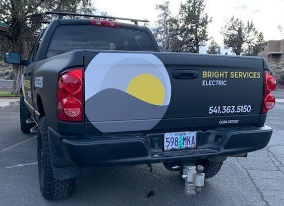 A black truck with a yellow sun on the back is parked in a parking lot.