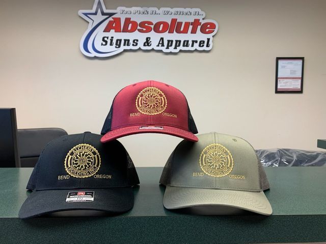 Three hats are on a counter in front of absolute signs & apparel